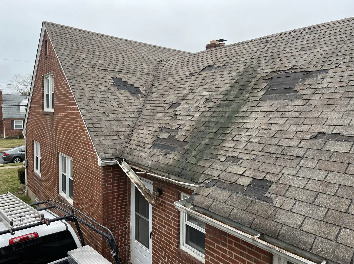 Worn, curling asphalt shingle roof with missing shingles on a brick twin home